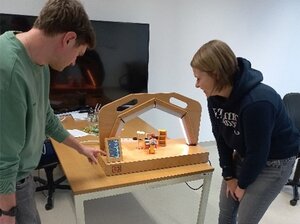 Zwei Personen vor einem Demonstrator aus Holz in Büroumgebung, mit einem Steuerungselement.