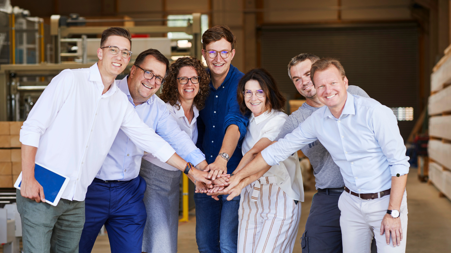 Gruppe von Menschen in einer Produktionshalle, die Hände übereinanderhalten